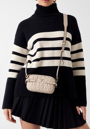 Czarno-biały sweter w paski z wysokim kołnierzem, zestawiony z beżową pikowaną torbą na ramię z błyszczącymi metalowymi elementami.