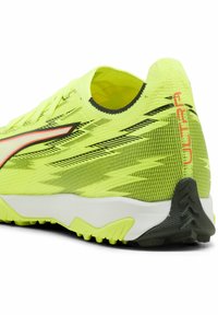 Neon gul træningssko med et struktureret mesh-overmateriale, sorte accenter og en hvid mellemsål. Har "ULTRA" i rødt på hælen og en gummieret ydersål.