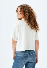 Camiseta de algodón blanca con mangas cortas, corte relajado y longitud cropped. Combinada con jeans de mezclilla azul que cuentan con un diseño clásico de cinco bolsillos.