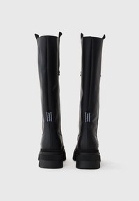 Knöchelhohe schwarze Gummistiefel mit matter Oberfläche, ausgestattet mit Ziehhilfen, robusten Sohlen und Branding an den Seiten. Texturiert für Grip und Langlebigkeit.