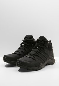 Czarne, wodoodporne buty trekkingowe z fakturowaną cholewką, wzmocnionym czubkiem i elastyczną gumową podeszwą. Posiadają bezpieczny system sznurowania oraz akcenty z logo.