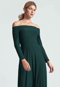 Off-shoulder, lange mouwen groene jurk van zachte stof, aansluitende lijfje, vloeiende rok. Heeft een gladde textuur en een strakke silhouette.