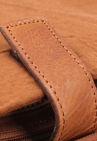 Cintura in pelle marrone con cuciture visibili, posizionata su uno sfondo di tessuto marrone texturizzato, evidenziando materiali e colori a contrasto.