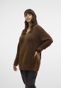 Brown oversized sweater made of soft, fuzzy material with a V-neck and long sleeves, paired with fitted black pants.