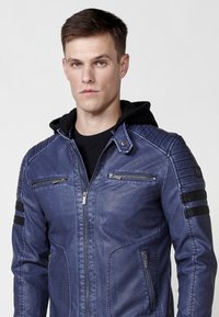 Chaqueta de imitación de cuero azul con cierre de cremallera frontal, dos bolsillos con cremallera en el pecho, acentos en los hombros y detalles de franjas negras en las mangas.