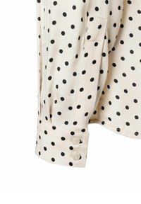 Crème blouse met zwarte polka dots, met een knoopmanchet en een gestroomlijnd silhouet. Zacht stof met een lichte glans.