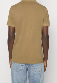 Kortärmad, olivgrön polotröja i bomull. Har en klassisk krage och ribbade ärmslut, bärs tillsammans med ljusblå denimjeans.