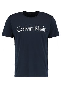 T-shirt en coton bleu marine avec col rond et manches courtes, arborant un grand texte blanc "Calvin Klein" centré sur le devant.
