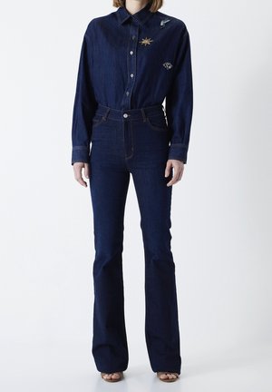 Chemise en denim bleu foncé avec col et fermeture à boutons, ornée de détails brodés. Associée à un jean en denim taille haute évasé.