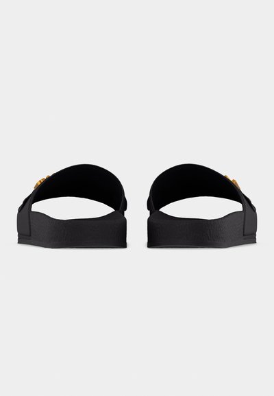 Ζευγάρι μαύρων σαγιοναρών με παχιά σόλα και φαρδιές λωρίδες, φωτογραφημένα από πίσω σε ανοιχτό φόντο.