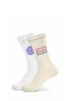 Deux chaussettes hautes côtelées, une blanche avec un visage souriant violet, l’autre beige avec le mot "amore" répété en rouge et bleu.