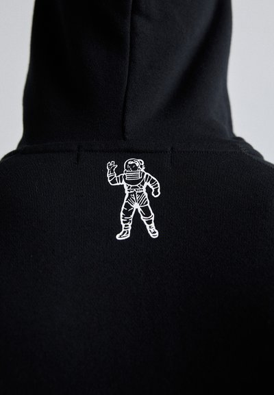 Sort hættetrøje med et hvidt broderet astronautgrafik på ryggen, der viser en vinkende gestus i et detaljeret rumdragt design.