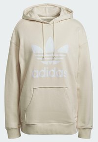 Béžová mikina s kapucí, klokaní kapsou, stahovací šňůrkou na kapuci a bílým logem Adidas s motivem trojlístku a třemi pruhy.