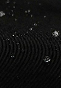 Tessuto nero con texture, con gocce d'acqua sparse sulla superficie, che evidenziano le sue proprietà idrorepellenti e la consistenza del materiale.