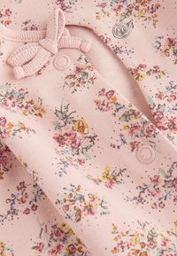 Tutina in tessuto rosa chiaro con motivo floreale in più colori, caratterizzata da un accento a fiocco testurizzato e bottoni a pressione sul davanti.