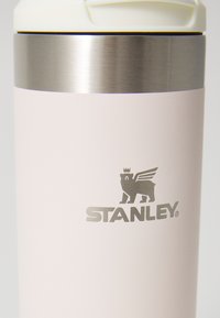 Gobelet isotherme en acier inoxydable de couleur rose doux avec une finition mate, une bande argentée et un logo STANLEY gravé avec un motif d'animal couronné.