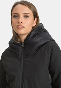 Czarna kurtka puchowa z podwójną teksturą, z błyszczącym kapturem i matowym tułowiem. Zamek błyskawiczny z przodu oraz minimalistyczny styl.