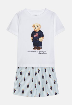 T-shirt de algodão branco com gráfico de urso em azul marinho, combinado com jeans. Calções às riscas azuis com estampado repetido de ursos em cores coordenadas.