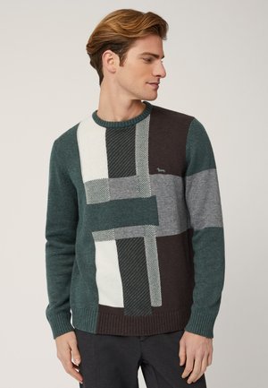Maglione a righe verdi, grigie e bianche con un punto testurizzato, caratterizzato da forme geometriche e un colletto e polsini a coste. Piccolo logo sul petto.