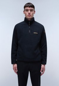 Pullover in pile nero con zip a metà, maniche raglan e una piccola etichetta con logo sul petto; texture liscia e vestibilità comoda.