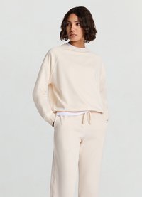 Sweat-shirt beige clair à col rond et manches raglan, associé à un pantalon à cordon de serrage assorti. Tissu doux, coupe décontractée.