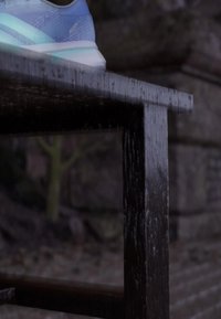Light blue running shoe with a mesh upper and reflective accents, resting on a dark wooden table with visible grain and water droplets.