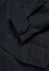 Close-up of black fabric showing two flap pockets with visible stitching on a garment.