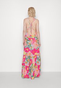 Vestido maxi floral con flores rosas, amarillas y naranjas sobre un fondo gris claro. Presenta un diseño sin espalda y volantes en capas.