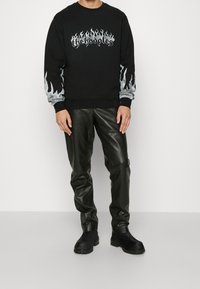 Svart sweatshirt med flammegrafik och texten "thehooples"; tillsammans med glänsande svarta läderbyxor och svarta ankellång stövlar.