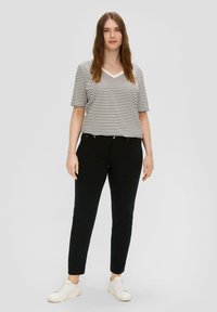  gestreepte v-hals t-shirt in crème en zwart, gecombineerd met strakke zwarte broek en witte sneakers. Eenvoudig ontwerp met korte mouwen en een losse pasvorm.