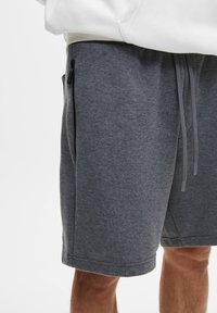 Shorts de sport gris en tissu texturé. Ils présentent une taille à cordon de serrage et une poche latérale zippée pour le rangement.