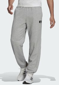 Graue Baumwoll-Sweatpants mit einem elastischen Bund und seitlichen Taschen. Mit einem kleinen schwarzen Logo-Patch auf dem linken Oberschenkel.