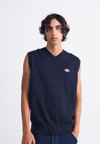 Suéter sin mangas en color marino con cuello en V, hecho de tejido de punto texturizado. Presenta un pequeño logotipo en el pecho y un dobladillo acanalado.