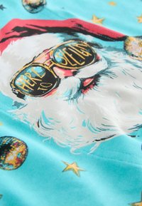 Krāsains audums ar Ziemassvētku vecīša dizainu, kas valkā saulesbrilles. Fons ir tirkīzzils ar dekoratīviem disko bumbām un dažādas krāsas zvaigznēm.