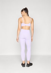 Bra sportivo lilla con spalline regolabili e chiusura a gancio, abbinato a leggings a vita alta coordinati. Modella indossa scarpe da ginnastica nere.