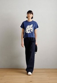 Ναυτικού μπλε βαμβακερό t-shirt με λευκή γραφική εικόνα μονόκερου, σε συνδυασμό με ψηλόμεσα σκούρα τζιν παντελόνια και λευκά αθλητικά παπούτσια. Απλή μαύρη τσάντα.