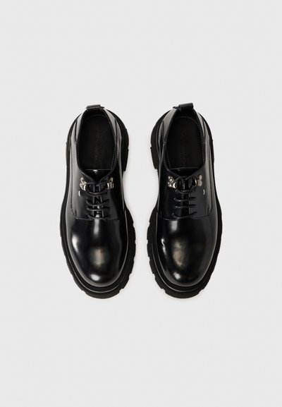 Chaussures noires en cuir avec une finition brillante, dotées d'un bout arrondi, d'un laçage et d'une épaisse semelle en caoutchouc. Pas de motifs ou d'ornements proéminents.