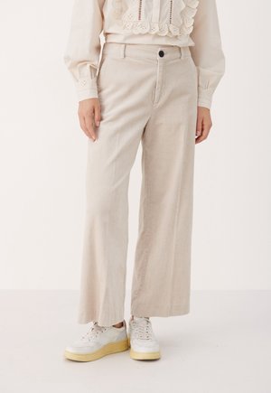 Beige weite Cordhosen, getragen mit weißen Sneakers und einer cremefarbenen Bluse mit Spitze und Ösen-Details.