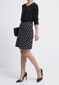 Blusa negra con detalles de botones combinada con una falda de lunares blancos y negros. Completan el look unos tacones negros de punta y un bolso negro.