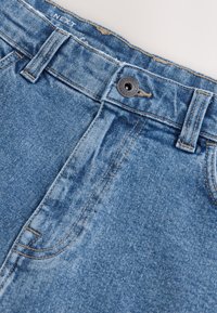 Jeans in denim azzurro chiaro con chiusura a bottone e cerniera, dettagli di lievi scoloriture e cuciture a contrasto lungo le cuciture.
