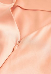 Pfirsichfarbene Seidenbluse mit glatter Textur, zarten Falten und einem kleinen Reißverschluss im Stoff.