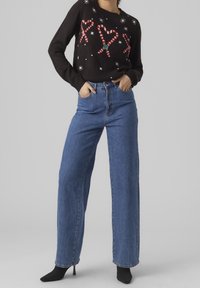Maglione nero con stampa di bastoncini di zucchero e fiocchi di neve, abbinato a jeans blu a vita alta e a gamba larga. Stivali neri con tacco completano l'outfit.