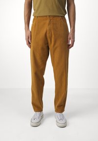 Pantalones de pana en color mostaza, con un ajuste relajado, bolsillos laterales y una textura suave, combinados con zapatillas blancas.