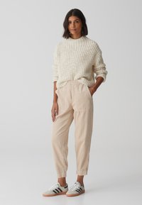 Pullover beige a coste con collo alto, abbinato a joggers in corduroy chiaro e sneakers grigie con strisce nere. Design minimalista, tessuto testurizzato.