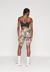 Μαύρο αθλητικό σουτιέν με σταυρωτή πλάτη, συνδυασμένο με πολύχρωμο ποδηλατικό σορτς με floral σχέδιο και κίτρινες πλευρικές ρίγες, λευκές κάλτσες και αθλητικά παπούτ σια.