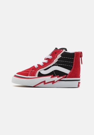 Zapatilla bota alta roja y negra con cordones blancos, una raya lateral blanca y un patrón de zigzag rojo en la suela blanca.