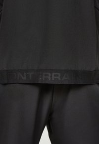 Gros plan sur un tissu noir montrant l'ourlet d'un vêtement avec un texte subtil "MONTERRA" embossé au niveau de la ceinture.