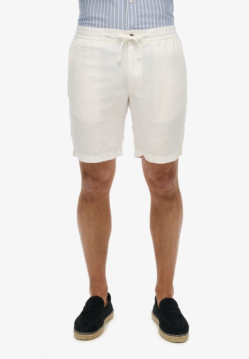 Weiße Leinen-Shorts mit einem elastischen Bund und Kordelzug. Glatte Textur, knielang, kombiniert mit schwarzen Espadrilles.
