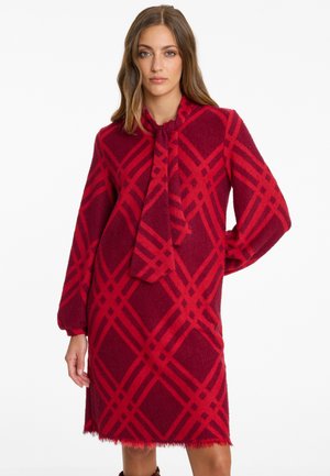 Robe écossaise rouge en tissu doux, avec des manches longues, un lien au cou et un ourlet à franges. Motif géométrique audacieux.