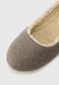 Chinelo cinza em feltro com forro e acabamento em fleece creme, mostrado de um ângulo superior próximo sobre um fundo branco.